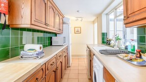 A kitchen with wooden cabinets, a microwave, a washing machine, and a sink with various items on the counter. - The Anchorage (Whitby)