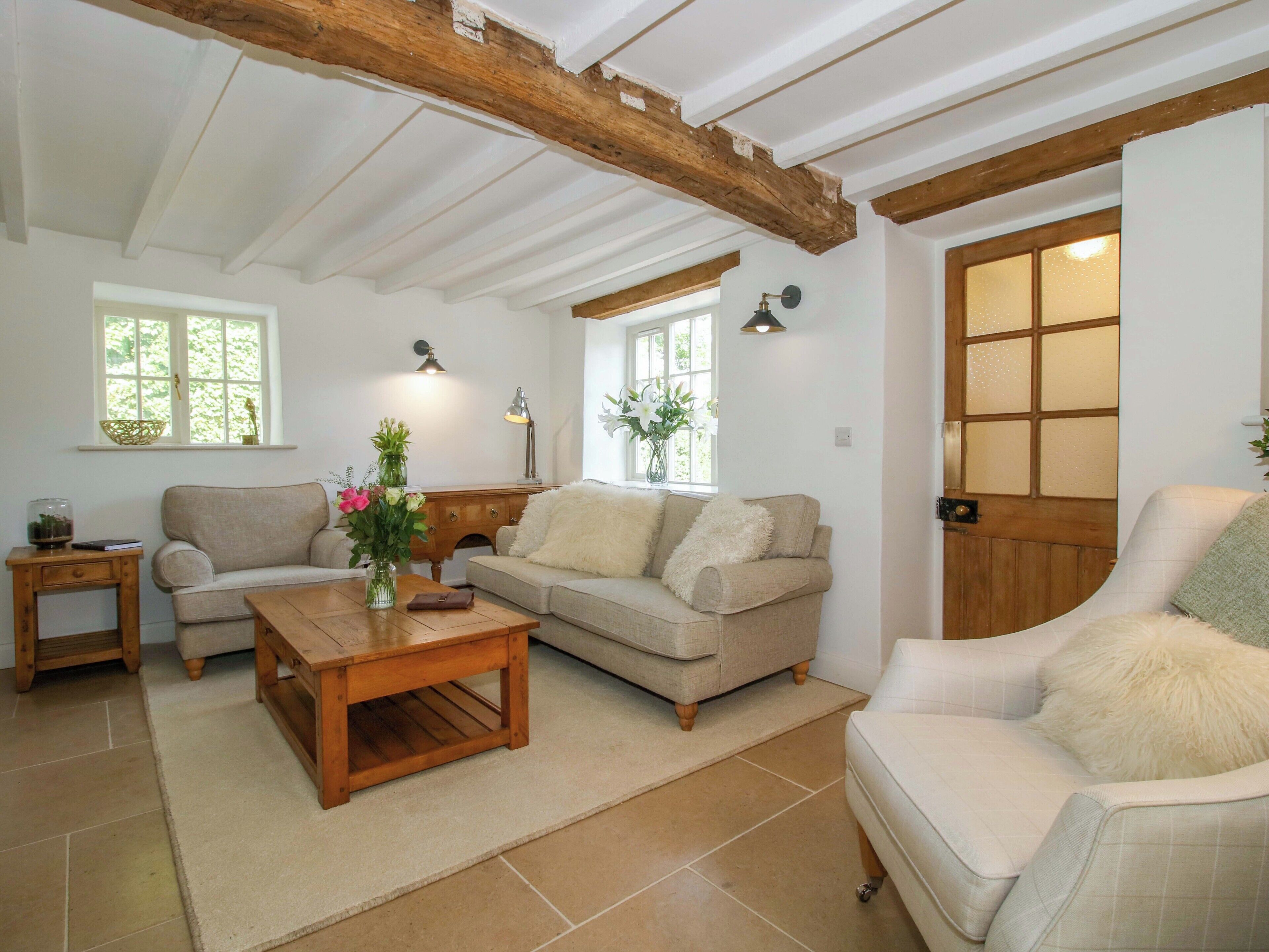 A cozy living room with a wooden ceiling, two sofas, a coffee table, and a side table with a vase of flowers.