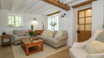 A cozy living room with a wooden ceiling, two sofas, a coffee table, and a side table with a vase of flowers.