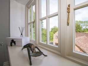 A room with large windows, a white table with a decorative item, and a view of a stone building outside. - 5 Shrewsbury Road (Much Wenlock)