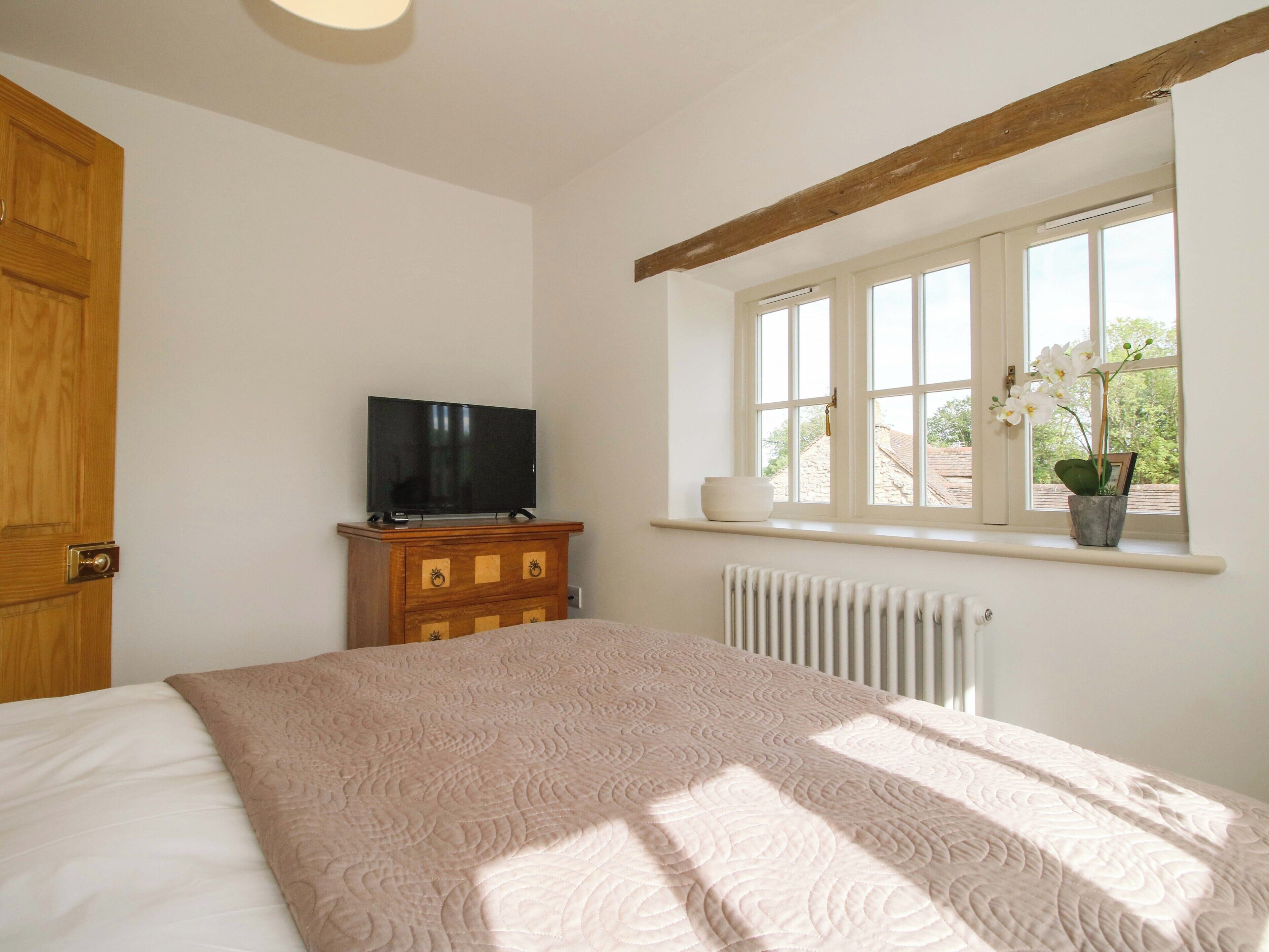 Un dormitorio con cama, cómoda, televisor, ventana con vistas y radiador.