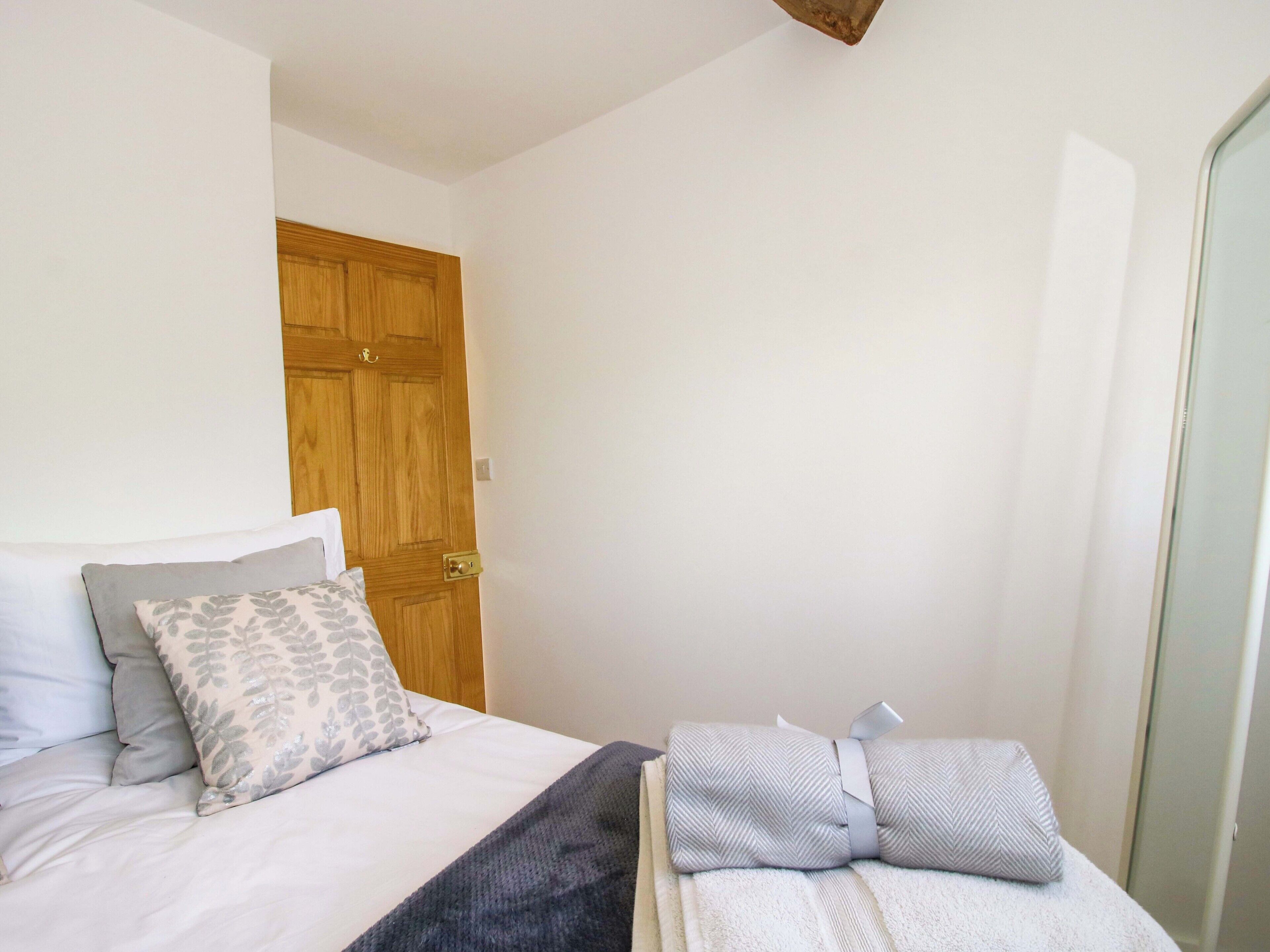 A bedroom with a bed, pillows, a blanket, a wooden door, and a mirror.