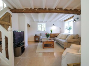A living room with a television, sofa, coffee table, and a wooden staircase. - 5 Shrewsbury Road (Much Wenlock)
