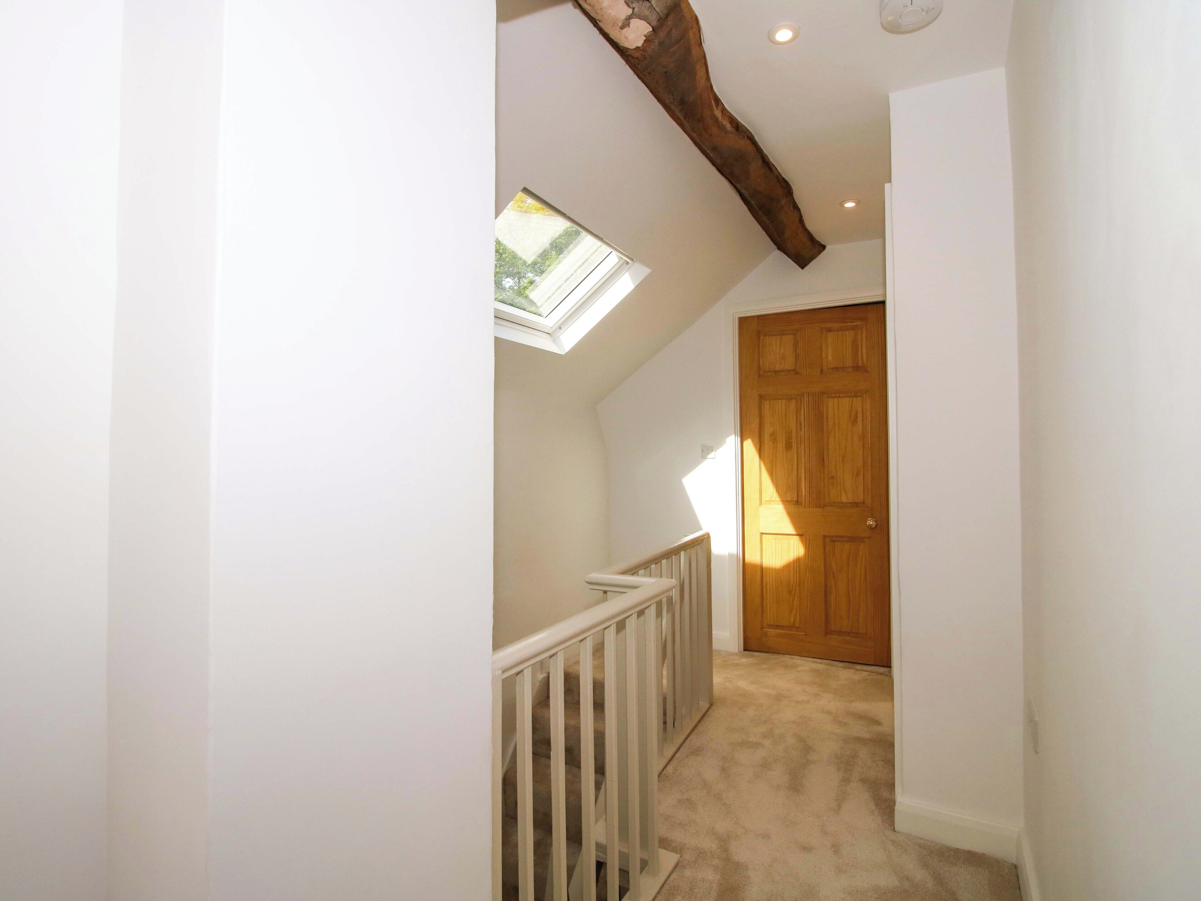A hallway with a wooden door, a white railing, and a skylight.