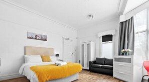 A modern hotel room with a bed, a sofa, a desk, and a window with curtains. - Private Ensuite Room in Shared Home with Kitchenette & Street Parking (West Yorkshire)