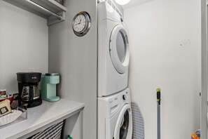 Un cuarto de lavandería con lavadora y secadora apiladas, una cafetera y un reloj en la pared.