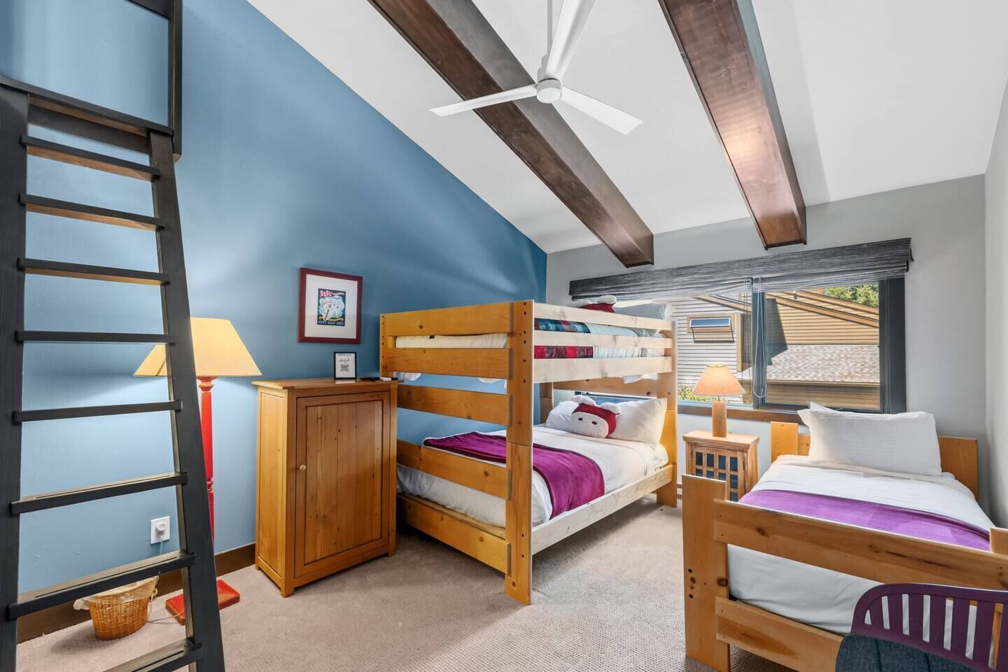 A bunk bed room with a ceiling fan, a wooden wardrobe, and a window with a view.