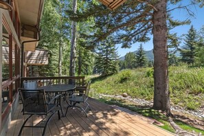Una terraza de madera con una mesa y sillas, rodeada de árboles y vistas a un paisaje montañoso.