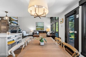 A spacious living room with a wooden dining table, comfortable seating, a large window, and a modern chandelier. - Peaceful Vail Family Retreat | Bus Access + Views (Vail)