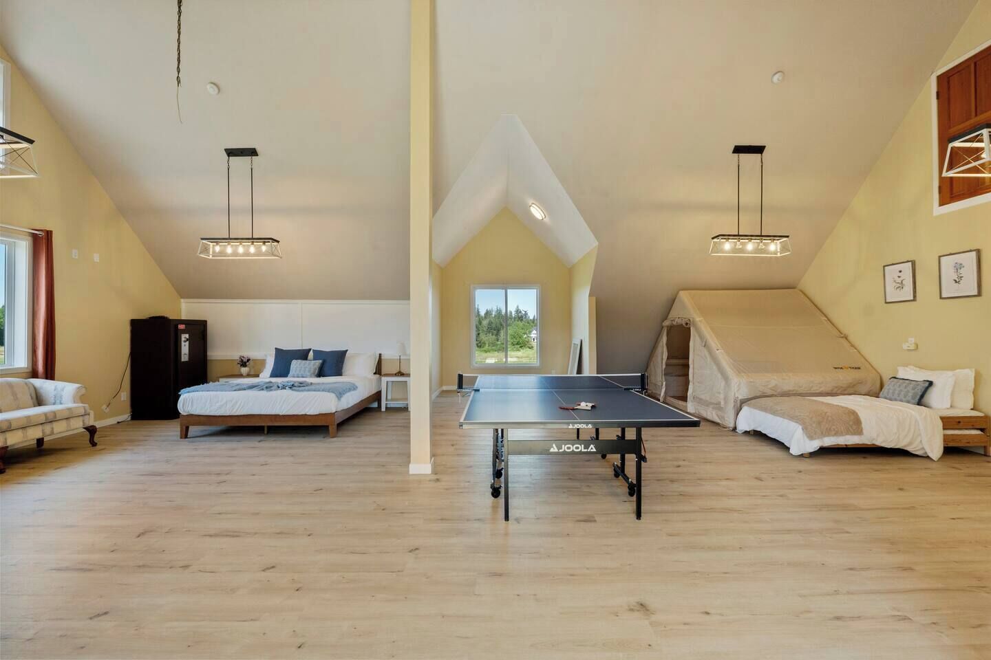 A spacious loft bedroom with a ping pong table, a bed, and a tent-like structure.