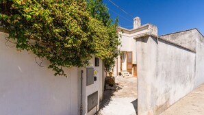 A narrow alleyway with a white building on the left, a concrete wall on the right, and a clear blue sky above.