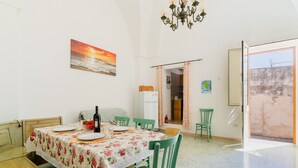 A dining area with a table set for two, a bottle of wine, and a painting of a sunset on the wall.