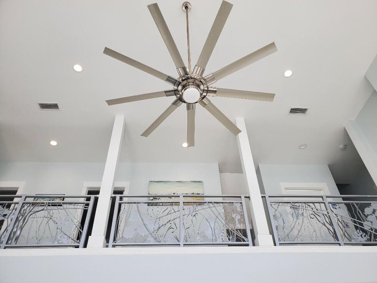 A modern interior with a central ceiling fan, white walls, and a balcony with metal railings.