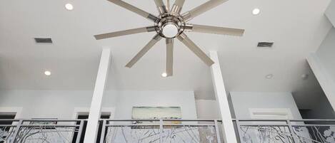 A modern interior with a central ceiling fan, white walls, and a balcony with metal railings.