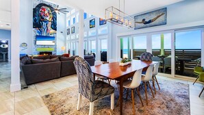 Een ruime woonkamer met een eettafel, bank en stoelen, grote ramen met uitzicht en een plafondventilator.