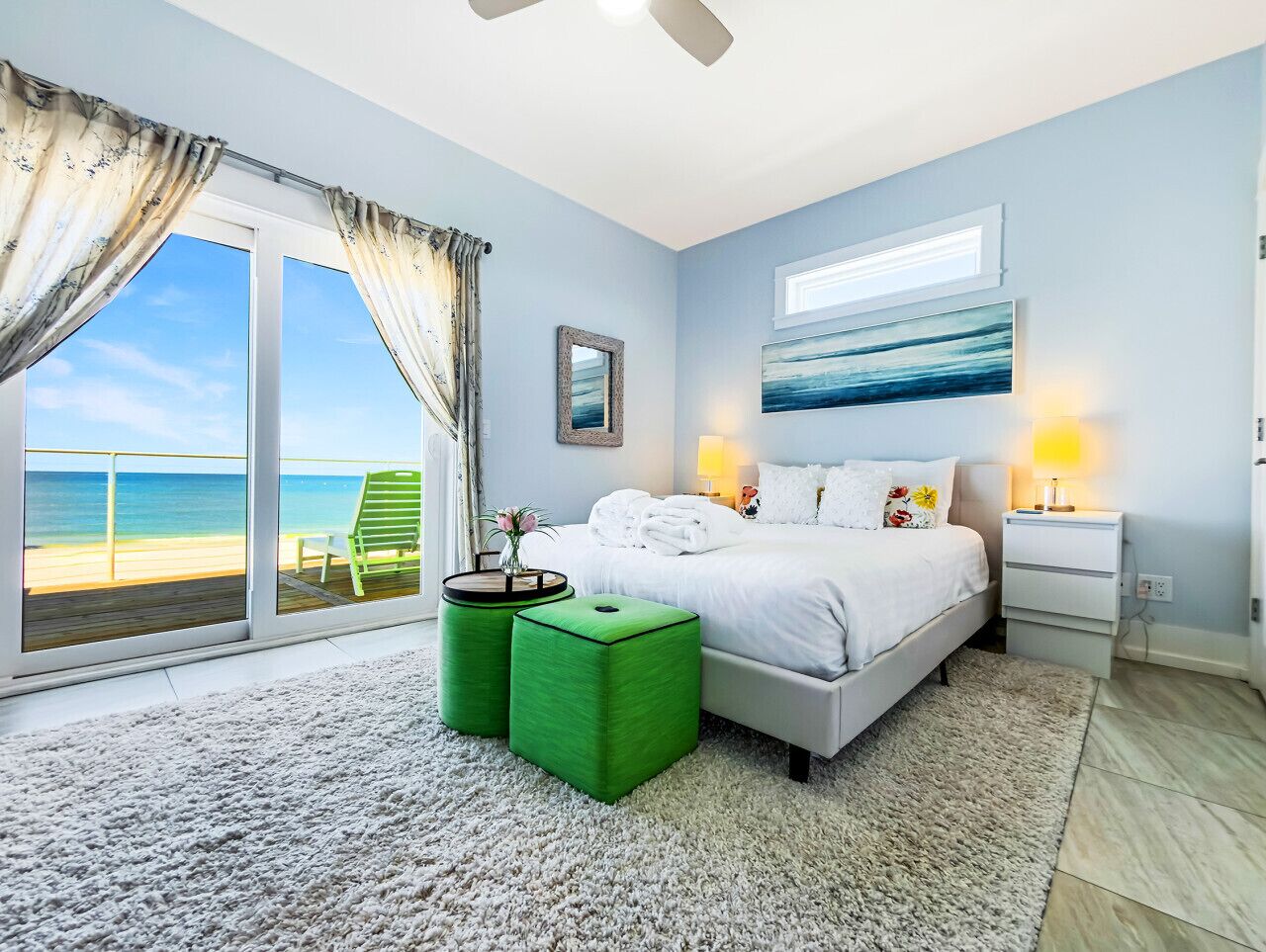 Une chambre à coucher avec un lit, une table de chevet, une lampe, un fauteuil vert et une vue sur la plage.