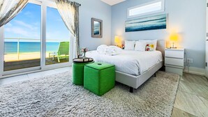Een slaapkamer met een bed, een nachtkastje, een lamp, een groene stoel en uitzicht op het strand.