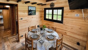 A wooden interior with a dining table set for four, a wooden floor, a window with a view, and a mounted television. - Nature & relaxation chalet near the Loire Castles (Rilly-sur-Loire)