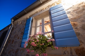 Ein Steinhaus mit Fenster und Fensterläden, einem Blumenkasten und blauem Himmel.