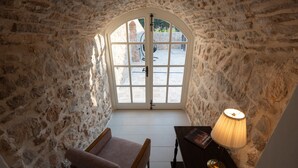 A stone-walled room with a large arched window, a chair, a table with a lamp, and a book. - Historic Stone House on Vir Island (Vir)