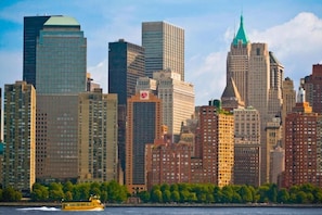 A city skyline with high-rise buildings, a river, and a yellow ferry. - New York Downtown Stay (New York)