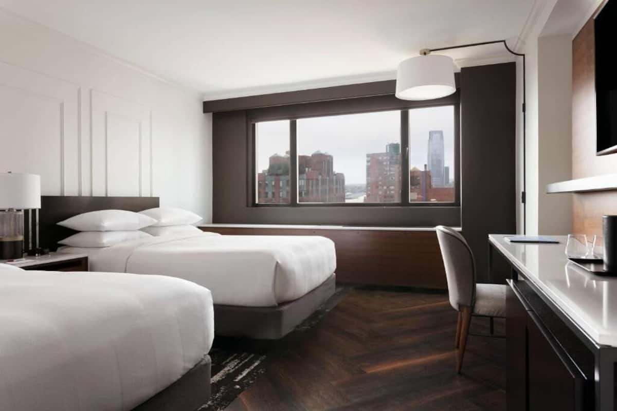 Habitación de hotel con dos camas, un escritorio, una silla, un ventanal con vistas a la ciudad y un televisor de pantalla plana.