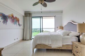 Een slaapkamer met een bed, nachtkastje, lamp, plafondventilator en een groot raam.