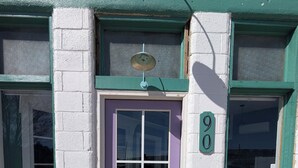 Un immeuble avec une porte violette, une plaque portant le numéro « 90 » et un paillasson sur lequel est écrit « bonjour ».