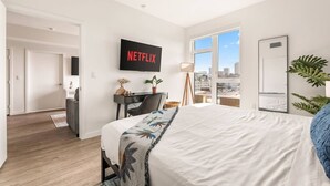 Une chambre d’hôtel moderne dotée d’un grand lit, d’un bureau avec une chaise, d’un téléviseur fixé au mur et offrant une vue sur la ville par la fenêtre.