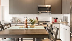 Une cuisine moderne avec des meubles de couleur sombre, un four à micro-ondes en acier inoxydable et une table à manger avec des chaises.