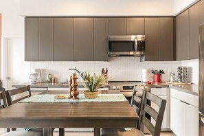 A modern kitchen with dark cabinets, a stainless steel microwave, and a dining table with chairs.