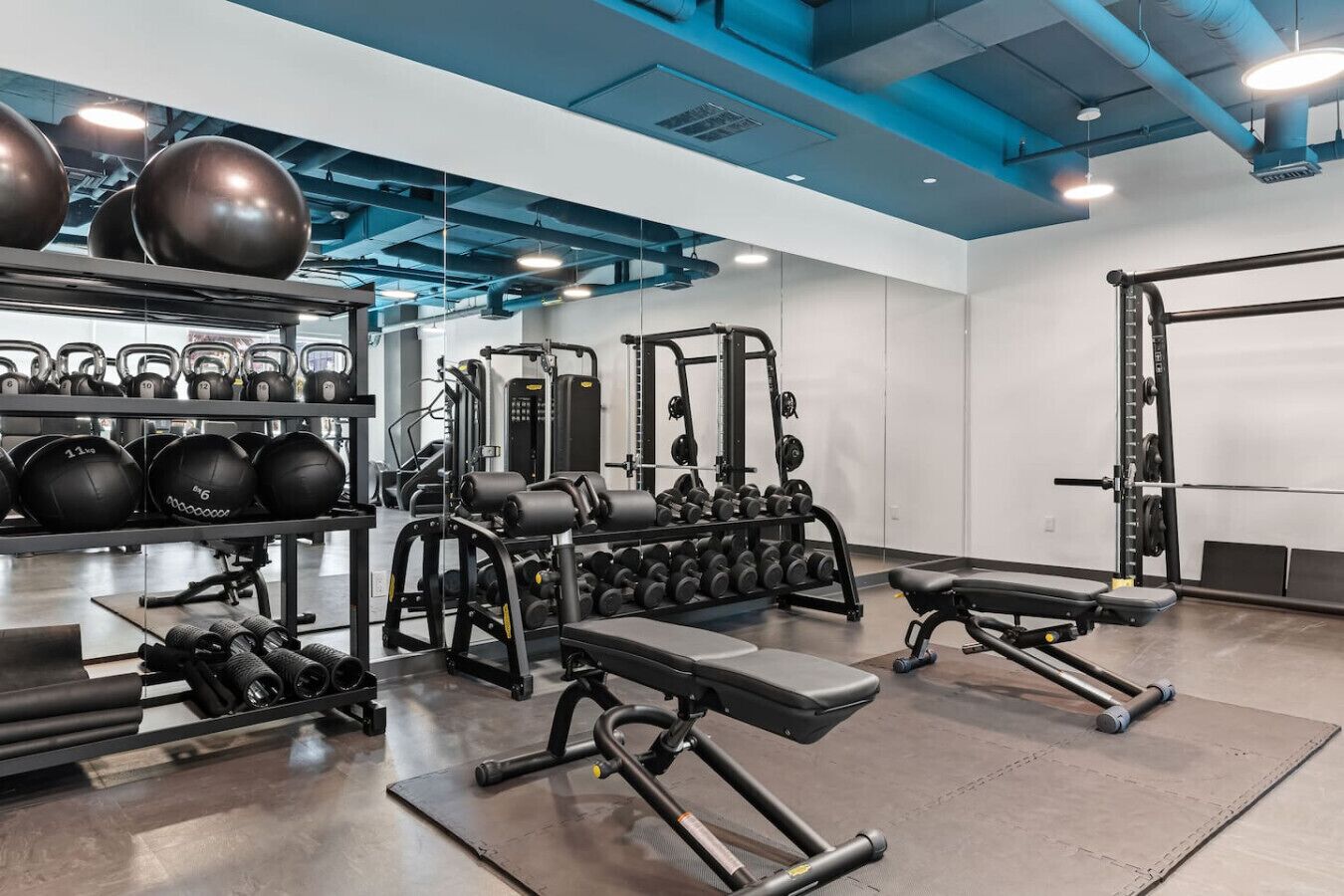 Un gimnasio con equipamiento de levantamiento de pesas, cintas de correr y pelotas de ejercicio.