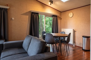 A cozy room with a sofa, a dining table with chairs, a clock on the wall, and a window with curtains. - Country Estate de Berghorst (Stegeren)