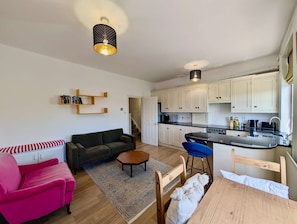 A compact living space with a kitchenette, a sofa, a dining table, and a staircase leading to an upper level. - Two bed flat near King s Cross St Pancras (London)