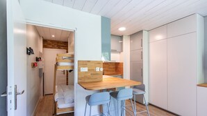 Una stanza funzionale con un letto a castello, un angolo cottura, un tavolo in legno con sgabelli da bar e un'armadio bianco.