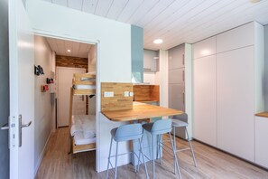 A compact room with a bunk bed, a small kitchenette, a wooden table with bar stools, and a white wardrobe. - Le Nid des Cimes - Proche de la navette des pistes (Barèges)
