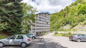 Un parcheggio con auto, un edificio dal design moderno e un pendio alberato.