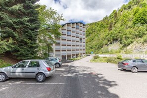 A parking lot with cars, a building with a modern design, and a hillside with trees. - Le Nid des Cimes - Proche de la navette des pistes (Barèges)