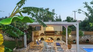 Um pátio externo com lareira de pedra, piscina e pérgola.