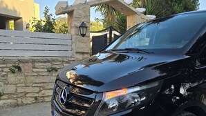 Um SUV preto Mercedes-Benz estacionado em frente a uma parede de pedra com um portão e um edifício ao fundo.