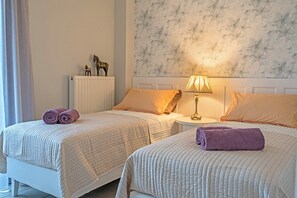 A hotel room with two beds, a radiator, a wall with a floral pattern, and a lamp on a bedside table. - Beautiful 4-bedroom resort with private swimming pool in charming Réthymno Crete (Atsipopoulo)