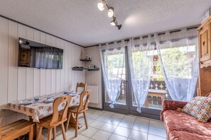 Ein Essbereich mit einem für zwei Personen gedecktem Tisch, Holzstühlen, einer Couch und einem Fenster mit Vorhängen.