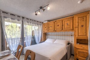 Ein Schlafzimmer mit einem Bett, Holzschränken, einem Tisch mit Tellern und einem Fenster mit Vorhängen.