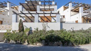 Un edificio moderno con facciata bianca, balconi in legno e un muro in pietra con piante sul davanti.