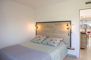 Ein Schlafzimmer mit Bett, zwei Wandlampen, einem Holz-Kopfteil und Blick auf einen Küchenbereich.