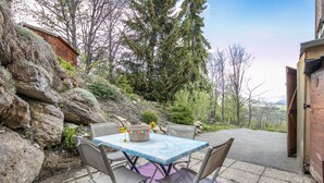 A patio with a table and chairs, a stone wall, and a wooden building. - Chez Sissi - Appt proche d'une remontée mécanique (Villarembert)