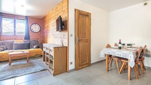 A cozy room with a sofa, a small table, a wooden cabinet, a dining table with chairs, and a clock on the wall. - Chez Sissi - Appt proche d'une remontée mécanique (Villarembert)