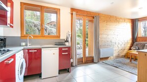 A compact kitchen with a washing machine, a coffee maker, and a dining area with a table and chairs. - Chez Sissi - Appt proche d'une remontée mécanique (Villarembert)