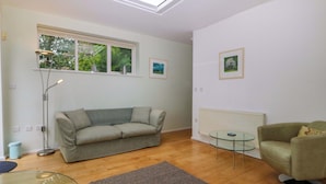 A living room with a sofa, a glass table, a floor lamp, and a radiator. - The Treehouse (Colwyn Bay)