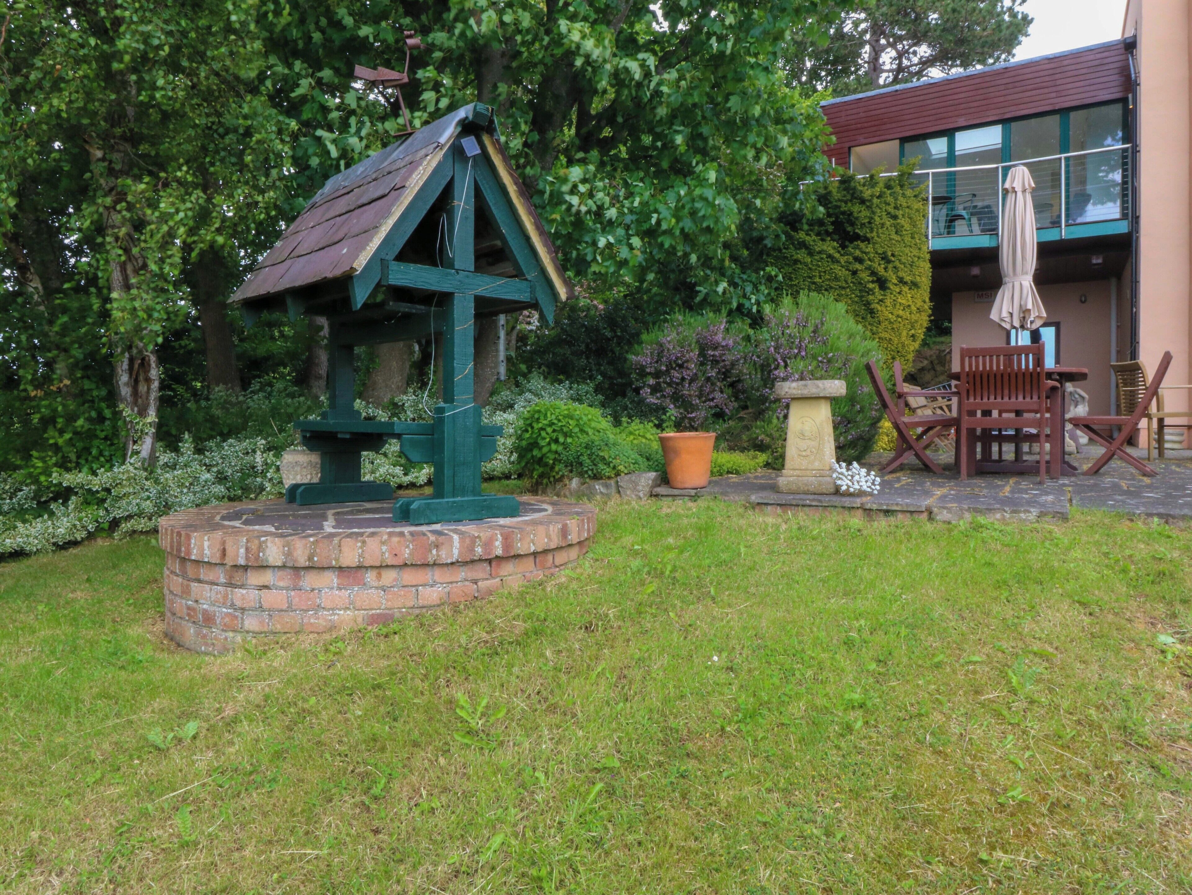 A garden with a birdhouse, a brick circular structure, a potted plant, and outdoor furniture.